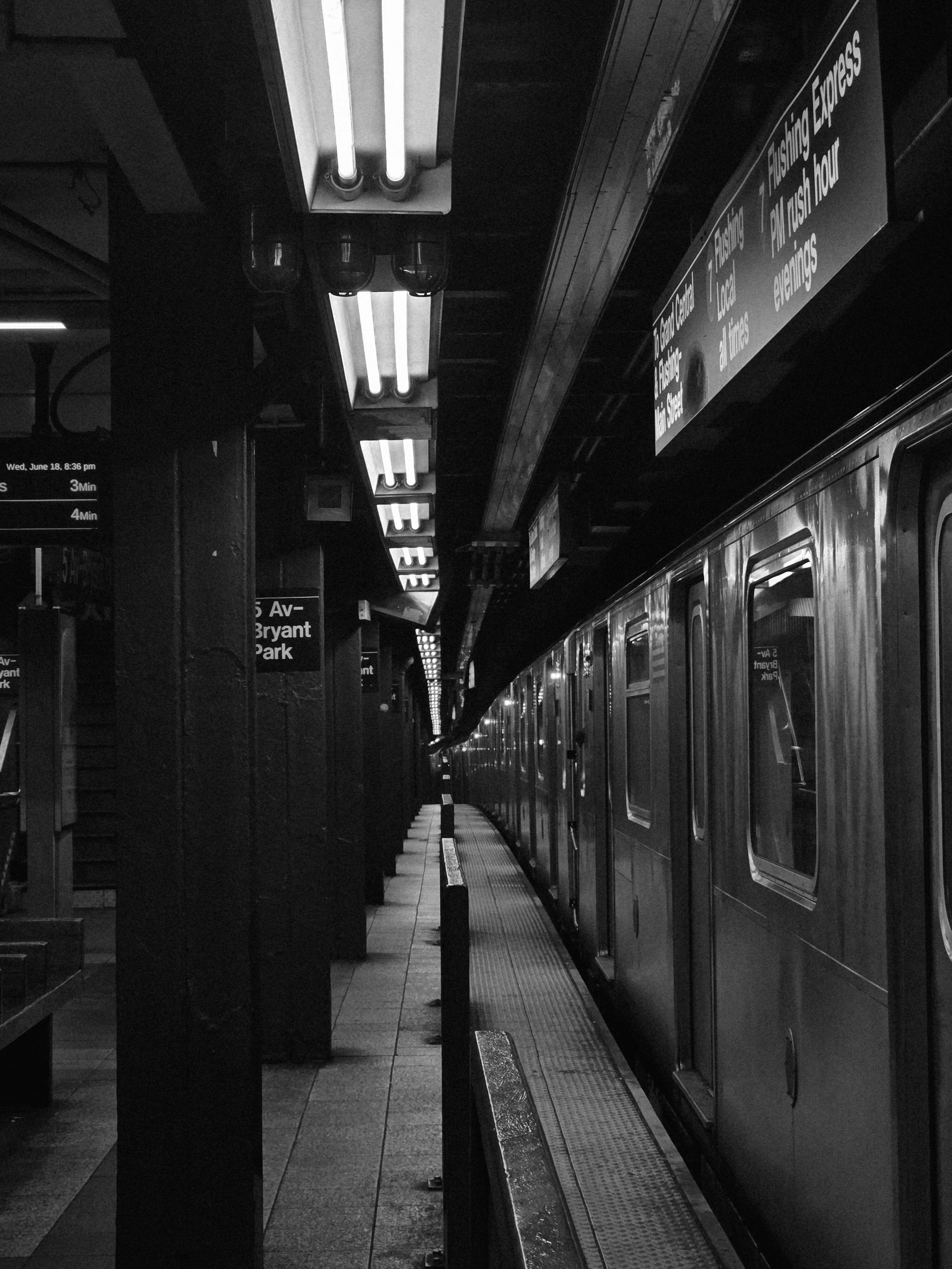 Black-and-white photograph of a New York City subway platform with a train and station signs